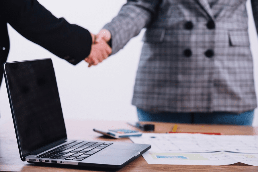 Laptop near people shaking hands Laptop near people shaking hands